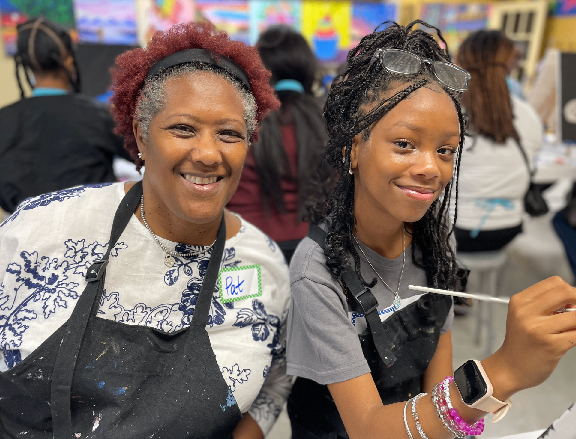 A mentor and mentee smiling together while painting in a creative workshop