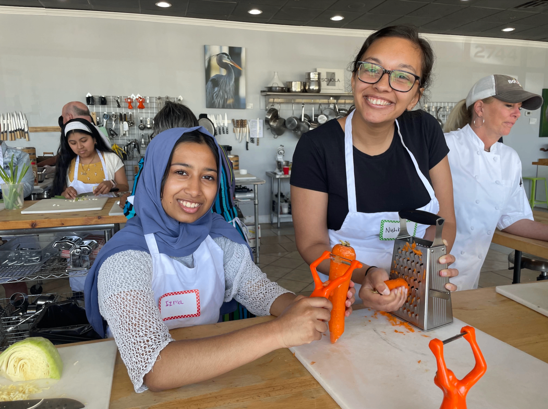 Two girls in aprons peeling and grating carrots in a kitchen
